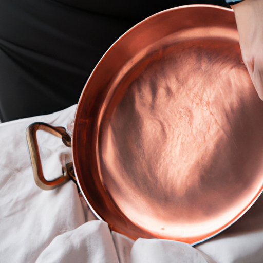 A close-up of a person polishing a copper frying pan with a soft cloth.